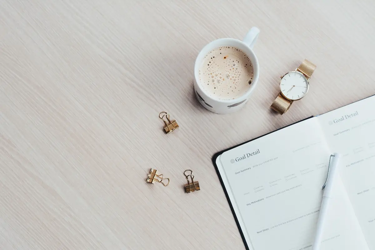 Desk with journal, coffee and watch. Someone establishing a routine.